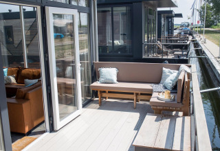 Buitenterras met zitbank en kussens op Waterlodge 4 aan de Zuiderzee in Nederland, uitzicht op kanaal.