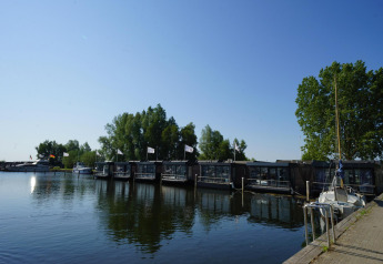 View of houseboats by a lakeside lodge, surrounded by trees and boats, under a clear blue sky.
