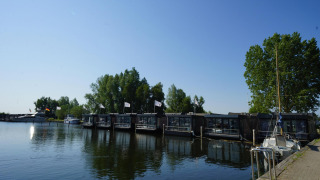 Hausboote am Ufer einer Lodge, umgeben von Bäumen und Booten, unter einem strahlend blauen Himmel.