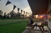 Hombre sentado en una mesa de picnic junto a una tienda glamping en De Regge-Vallei, Países Bajos al atardecer.