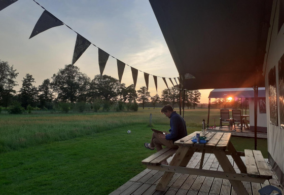 Mand sidder ved et picnicbord ved en glamping safari-teltplads i solnedgang på De Regge-Vallei, Holland.