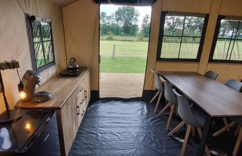 Interior de una tienda glamping safari en CharmeCamping De Regge-Vallei con cocina y comedor y campo.