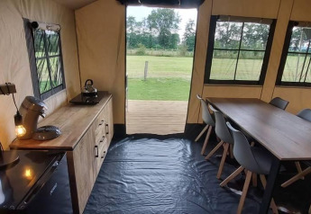 Indvendig udsigt over en luksuriøs glamping safari-telt med spisebord, køkken og udsigt til det grønne.