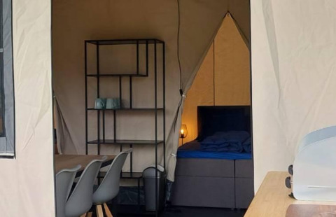 Interior de una tienda tipo safari glamping con área de comedor, estantería y cama en De Regge-Vallei, Países Bajos.