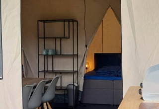 Interno di una tenda safari glamping con tavolo da pranzo, scaffale e letto a De Regge-Vallei, Paesi Bassi.