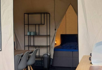 Interno di una tenda safari glamping con tavolo da pranzo, scaffale e letto a De Regge-Vallei, Paesi Bassi.