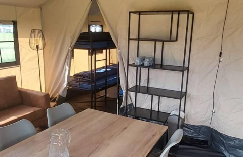 Interior de tienda de safari glamping con literas, mesa de comedor, estantería y sofá en De Regge-Vallei.