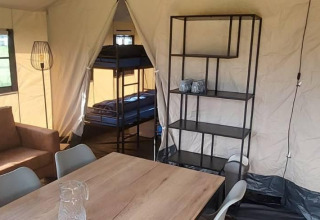 Intérieur d'une tente safari glamping avec lits superposés, table à manger, étagère et canapé à De Regge-Vallei.