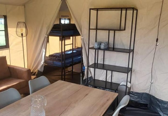 Interior de tienda de safari glamping con literas, mesa de comedor, estantería y sofá en De Regge-Vallei.