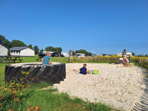 Børn leger i en sandkasse ved Glamping-telt på CharmeCamping De Regge-Vallei i Holland, solrig dag.