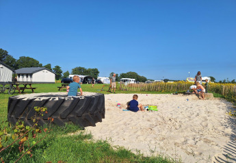 Børn leger i en sandkasse ved Glamping-telt på CharmeCamping De Regge-Vallei i Holland, solrig dag.