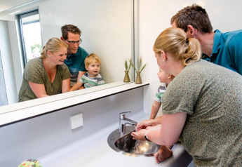 Una familia se lava las manos junta en un alojamiento glamping, sonriendo ante el espejo y el lavabo.