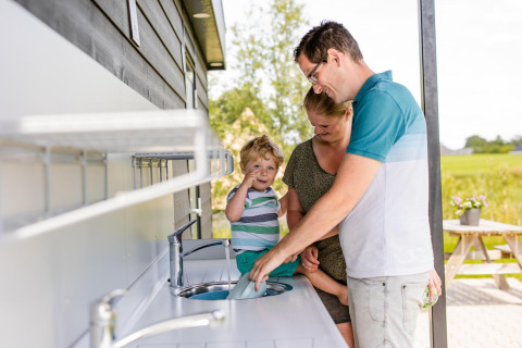 Una familia se lava las manos junta en un lavabo exterior en un alojamiento de glamping rural.