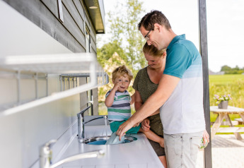 Una familia se lava las manos junta en un lavabo exterior en un alojamiento de glamping rural.