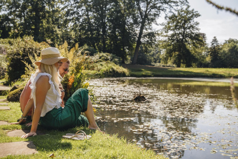 Dos personas descansan junto a un estanque tranquilo en un alojamiento glamping rodeado de naturaleza.