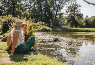 Twee personen genieten aan de rand van een vijver tijdens een glampingverblijf in het groen.