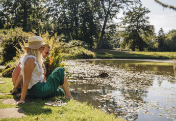Twee personen genieten aan de rand van een vijver tijdens een glampingverblijf in het groen.
