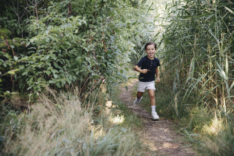 Un niño sonriente corre por un sendero rodeado de césped y arbustos, captado junto a una tienda safari.