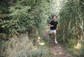Un niño sonriente corre por un sendero rodeado de césped y arbustos, captado junto a una tienda safari.