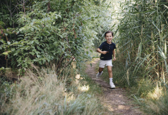 Un niño sonriente corre por un sendero rodeado de césped y arbustos, captado junto a una tienda safari.