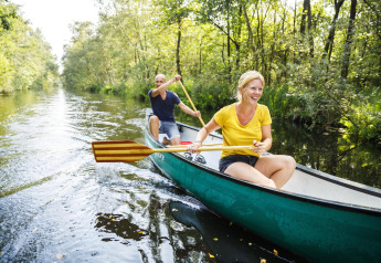 Coppia fa canoa su un fiume soleggiato tra alberi, durante una vacanza glamping immersa nella natura.
