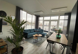 Sala de estar en la Waterlodge 6, Zuiderzee, Países Bajos, con sofá azul, gran ventanal y vista al puerto.