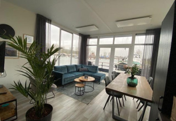 Stue i Waterlodge 6 ved Zuiderzee, Holland, med store vinduer, blå sofa og udsigt over havnen.
