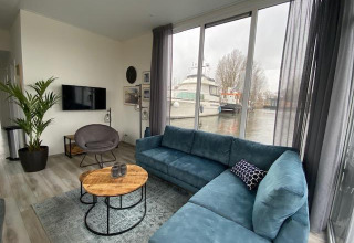 Salón moderno en Waterlodge 6, Zuiderzee, Países Bajos, con sofá azul y ventanales frente al agua.