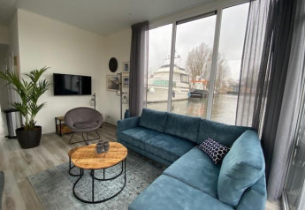 Stilfuld stue i Waterlodge 6 ved Zuiderzee, Nederlandene, med udsigt til vand og en moderne sofa.