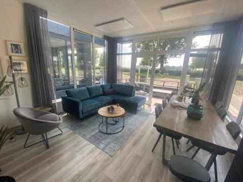 Wohnzimmer in Waterlodge 6 am Zuiderzee, Niederlande, mit großen Fenstern, Sofa und Esstisch.