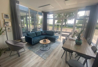 Wohnzimmer in Waterlodge 6 am Zuiderzee, Niederlande, mit großen Fenstern, Sofa und Esstisch.