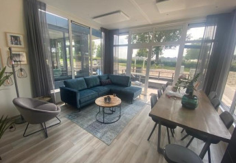Wohnzimmer in Waterlodge 6 am Zuiderzee, Niederlande, mit großen Fenstern, Sofa und Esstisch.