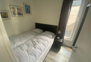 Schlafzimmer mit Doppelbett, Nachttisch und Fenster in Waterlodge 6 am Zuiderzee, Niederlande, modern eingerichtet.