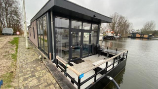Moderne waterlodge bij Zuiderzee in Nederland, op het water met glazen gevels en een houten terras.