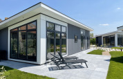 Lodge moderno Premium en Kompas Camping - Westende, Bélgica, con terraza soleada y sillas reclinables.