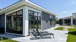 Moderne Premium Lodge im Kompas Camping - Westende, Belgien, mit Terrasse und Liegestühlen bei Sonnenschein.