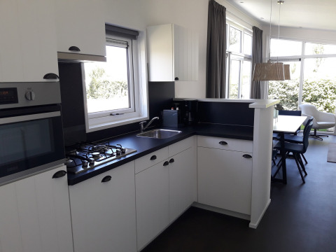 Moderne køkken med hvide skabe, sort bordplade og spiseområde i Premium Lodge ved Kompas Camping Westende.