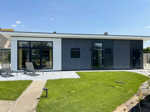 Premium Lodge ved Kompas Camping - Westende i Belgien med moderne facade, grøn græsplæne og liggestole.