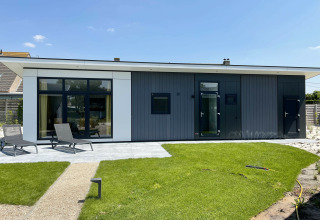 Premium Lodge bij Kompas Camping - Westende in België met moderne gevel, groene tuin en ligstoelen buiten.