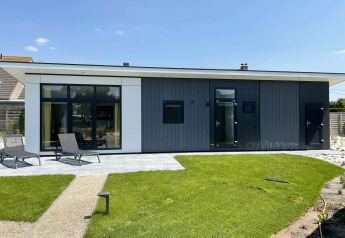 Premium Lodge en Kompas Camping - Westende, Bélgica, con diseño moderno, césped verde y tumbonas afuera.