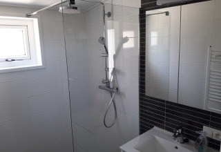 Moderne badkamer met glazen douchewand en regendouche in Premium Lodge bij Kompas Camping, Westende, België.