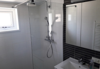 Moderne badkamer met glazen douchewand en regendouche in Premium Lodge bij Kompas Camping, Westende, België.
