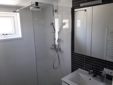 Baño moderno con ducha de vidrio y rociador tipo lluvia en Premium Lodge de Kompas Camping, Westende, Bélgica.