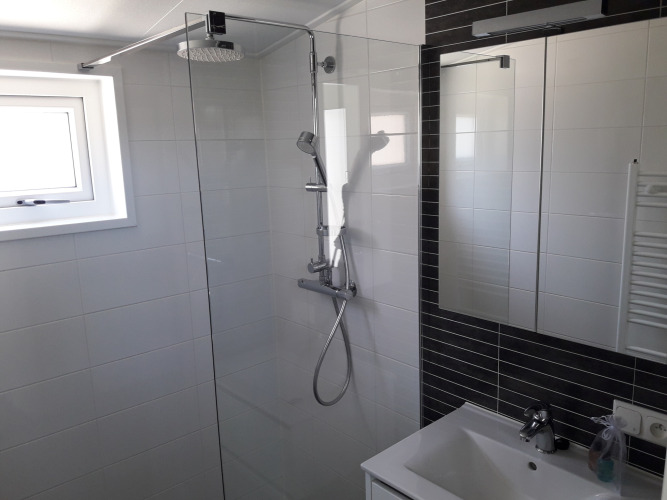 Baño moderno con ducha de vidrio y rociador tipo lluvia en Premium Lodge de Kompas Camping, Westende, Bélgica.