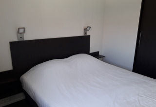 Dormitorio moderno en Premium Lodge de Kompas Camping - Westende, Bélgica, con cama doble y decoración minimalista.