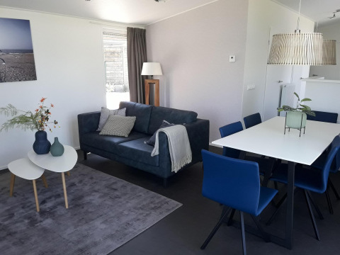 Modern living and dining area in Premium Lodge at Kompas Camping - Westende, Belgium, with blue sofa and chairs.