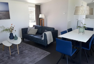 Modern living and dining area in Premium Lodge at Kompas Camping - Westende, Belgium, with blue sofa and chairs.