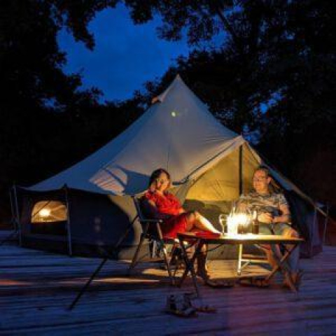 Zwei Personen entspannen vor einem beleuchteten Luxe-Bellzelt auf CharmeCamping De Regge-Vallei, Niederlande.