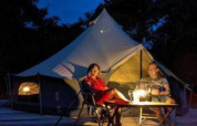 To personer slapper af foran et oplyst tipitelte ved CharmeCamping De Regge-Vallei i Holland om aftenen.