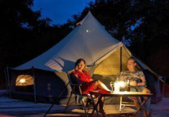 Due persone si rilassano davanti a una tenda a campana Luxe illuminata a CharmeCamping De Regge-Vallei, Paesi Bassi.